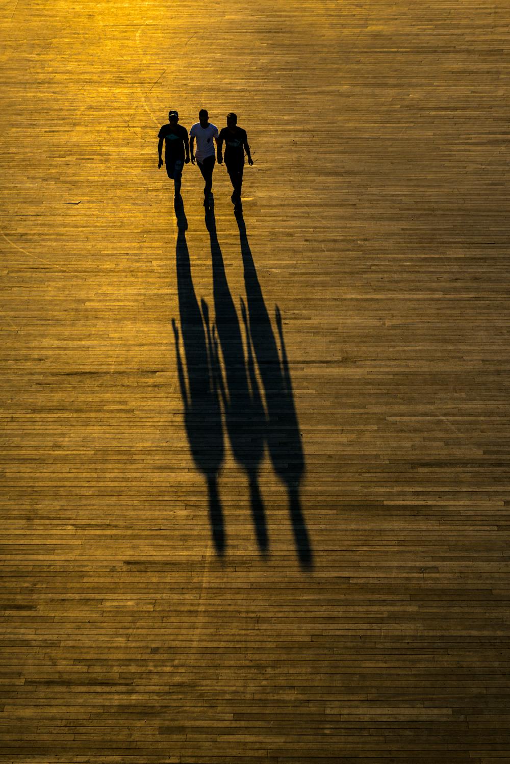 Three people walking down a street at sunset, casting long shadows on cobblestones. Shadow angle and length are unforgiving — given a known location, the sun's position on any given date is fixed within minutes. Photo by yavuz pancareken on Pexels.